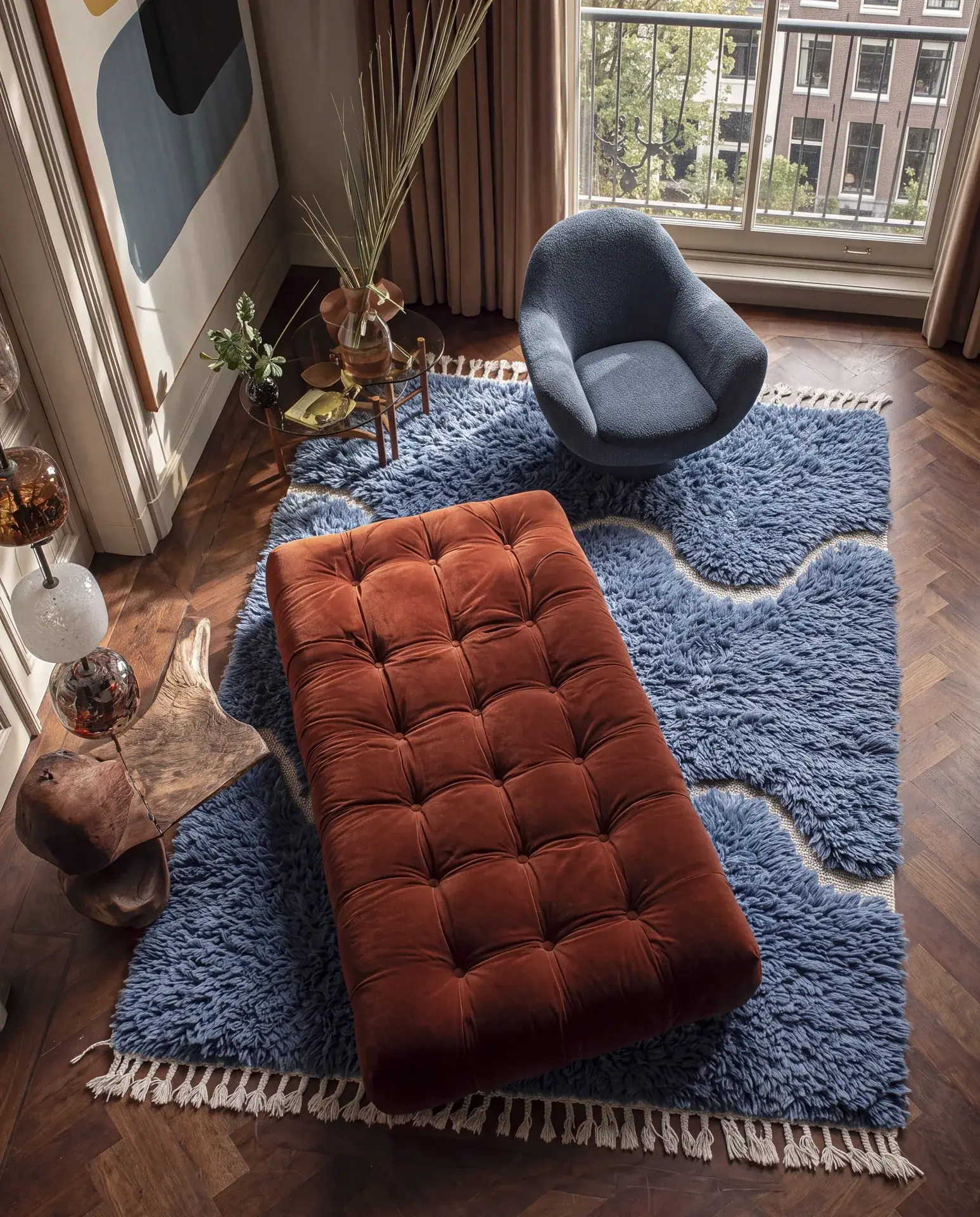 Draa Blue hand-knotted Moroccan rug in a living room beside a rust velvet ottoman and a blue chair