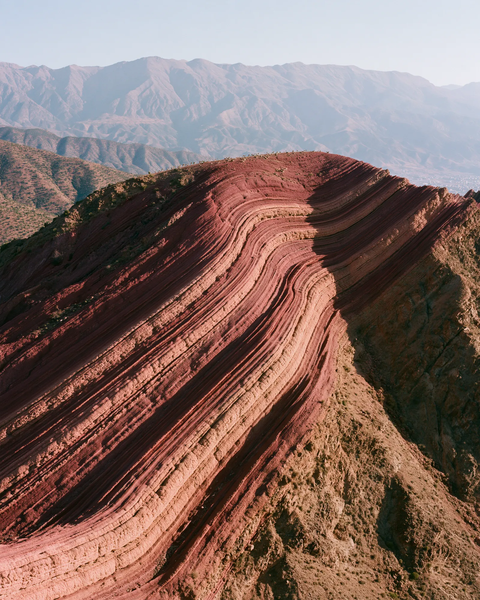 A rounded hill wrapped in rust and peach rock bands, the inspiration for the Aghbalou Rust & Peach rug