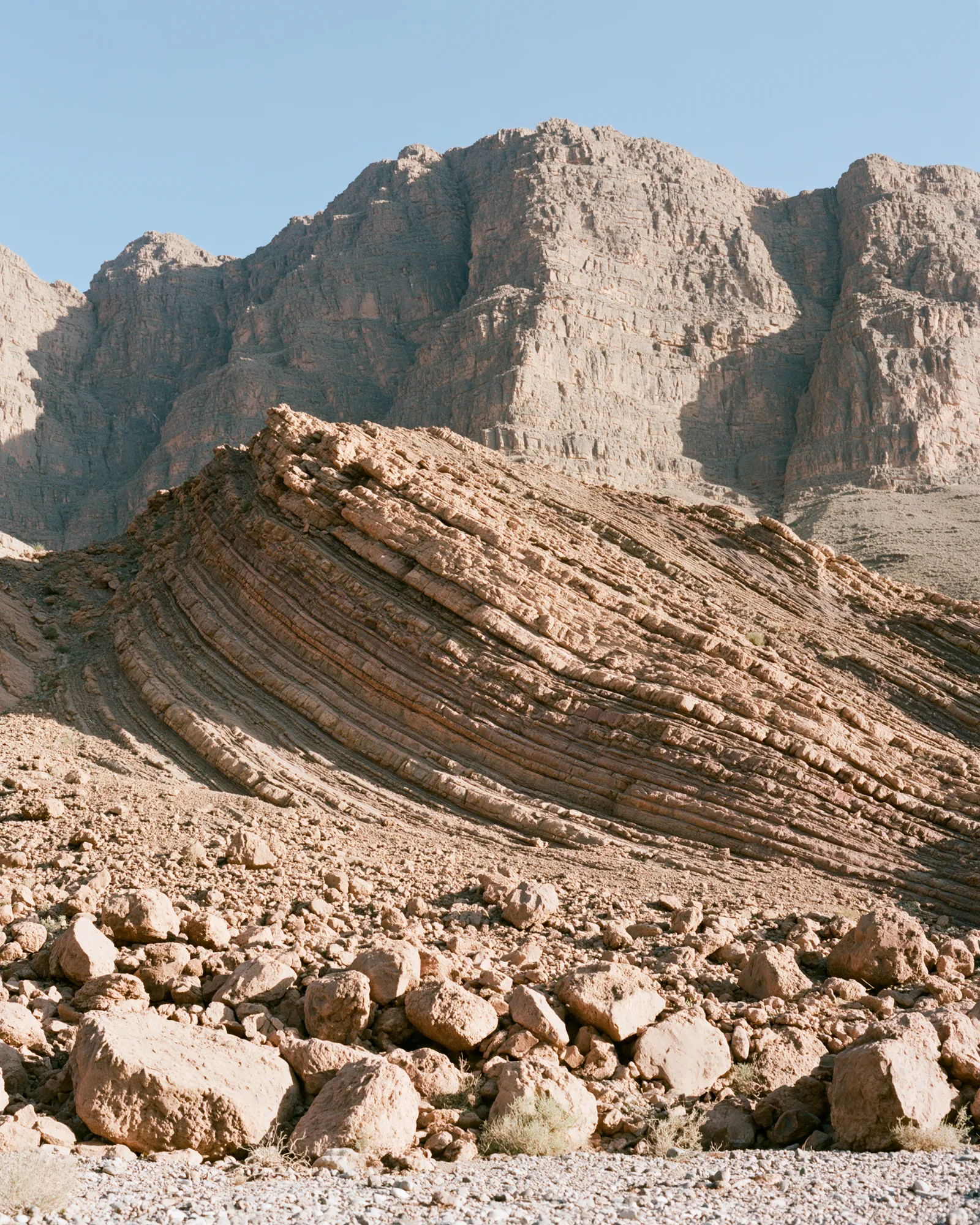 Tilted layers of rock on a desert hillside, the inspiration for the Dades Burgundy & Dusty Rose rug