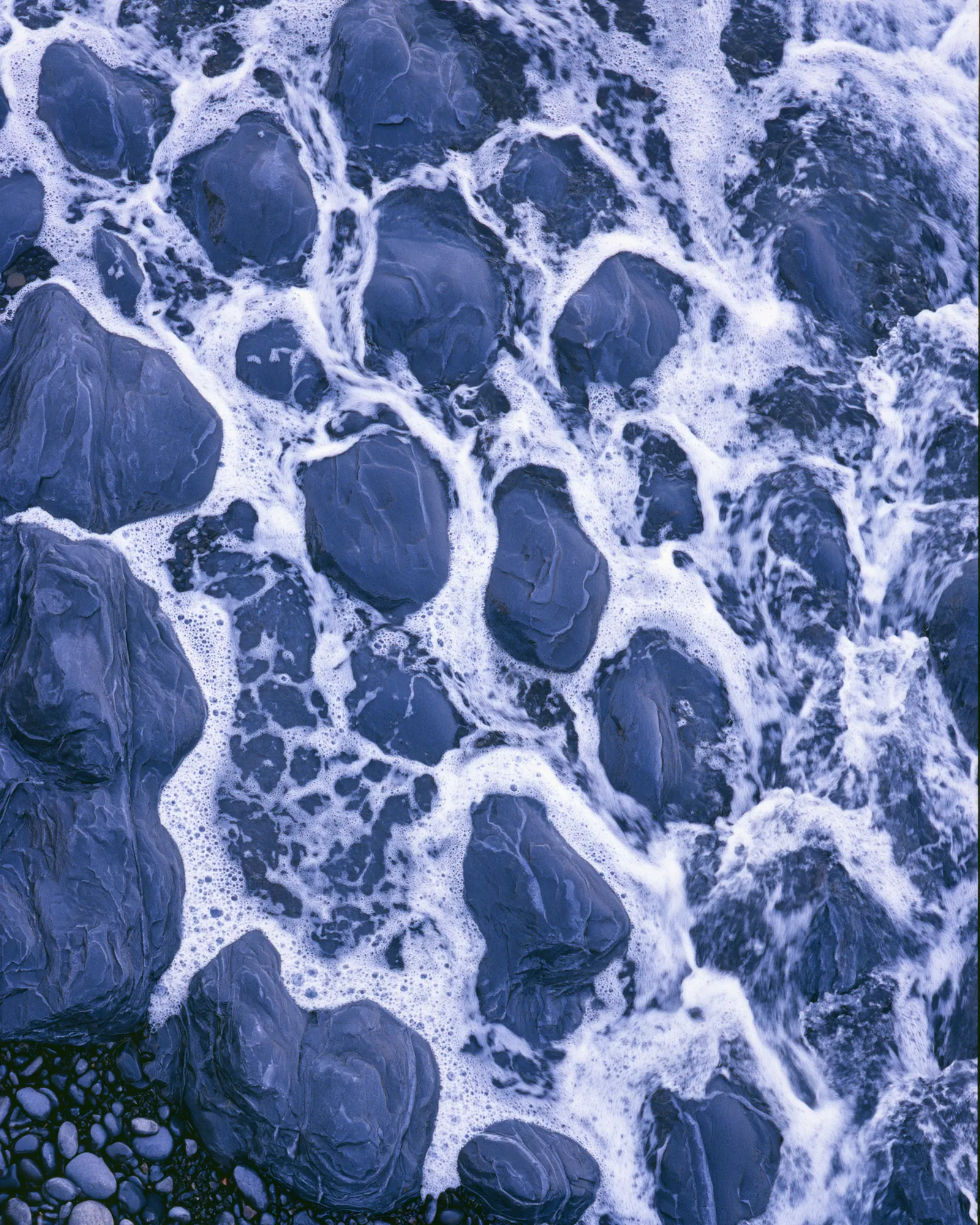 Blue stones in a shallow river with white foam running between them, the inspiration for the Ouzoud Blue & Ivory rug