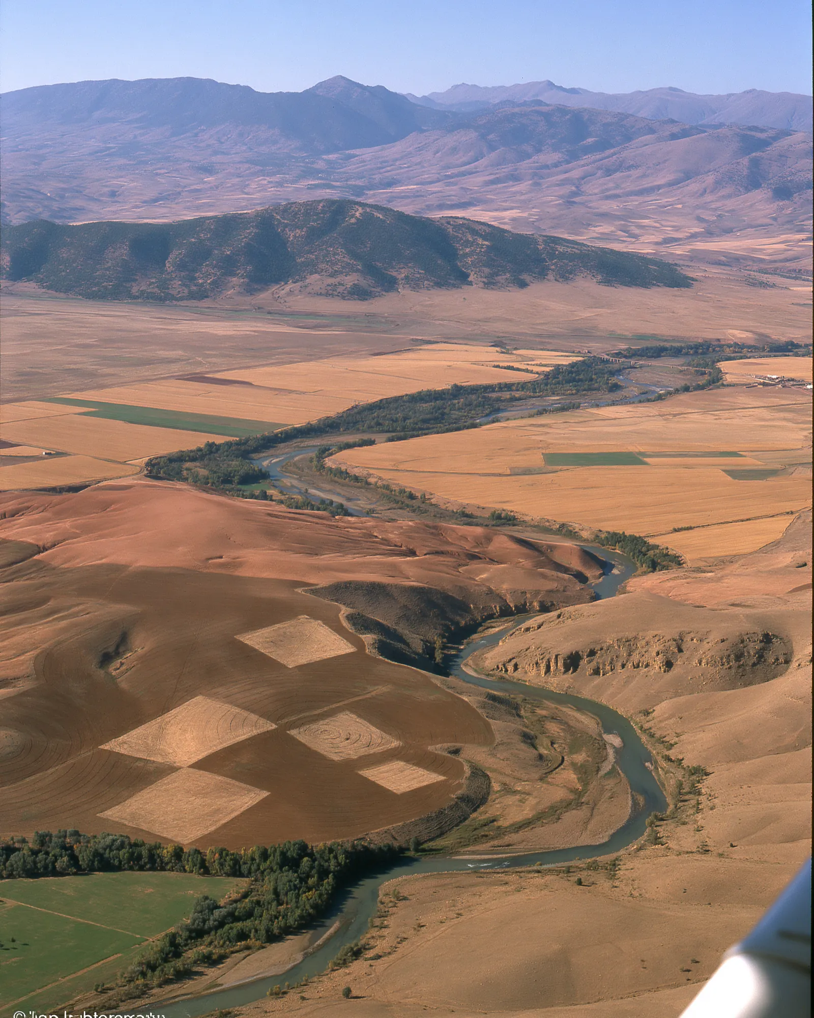 Aerial view of a river valley with checkered brown and gold fields, the inspiration for the Ronda Chocolate & Dusty Rose rug
