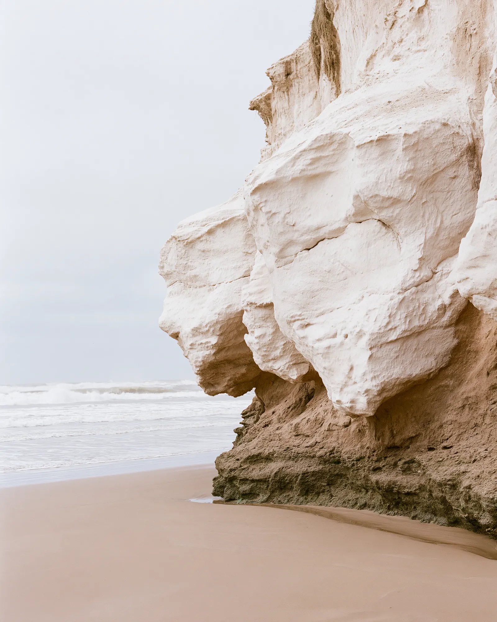 A pale sandstone cliff above a sandy beach, the inspiration for the Skala Ivory rug