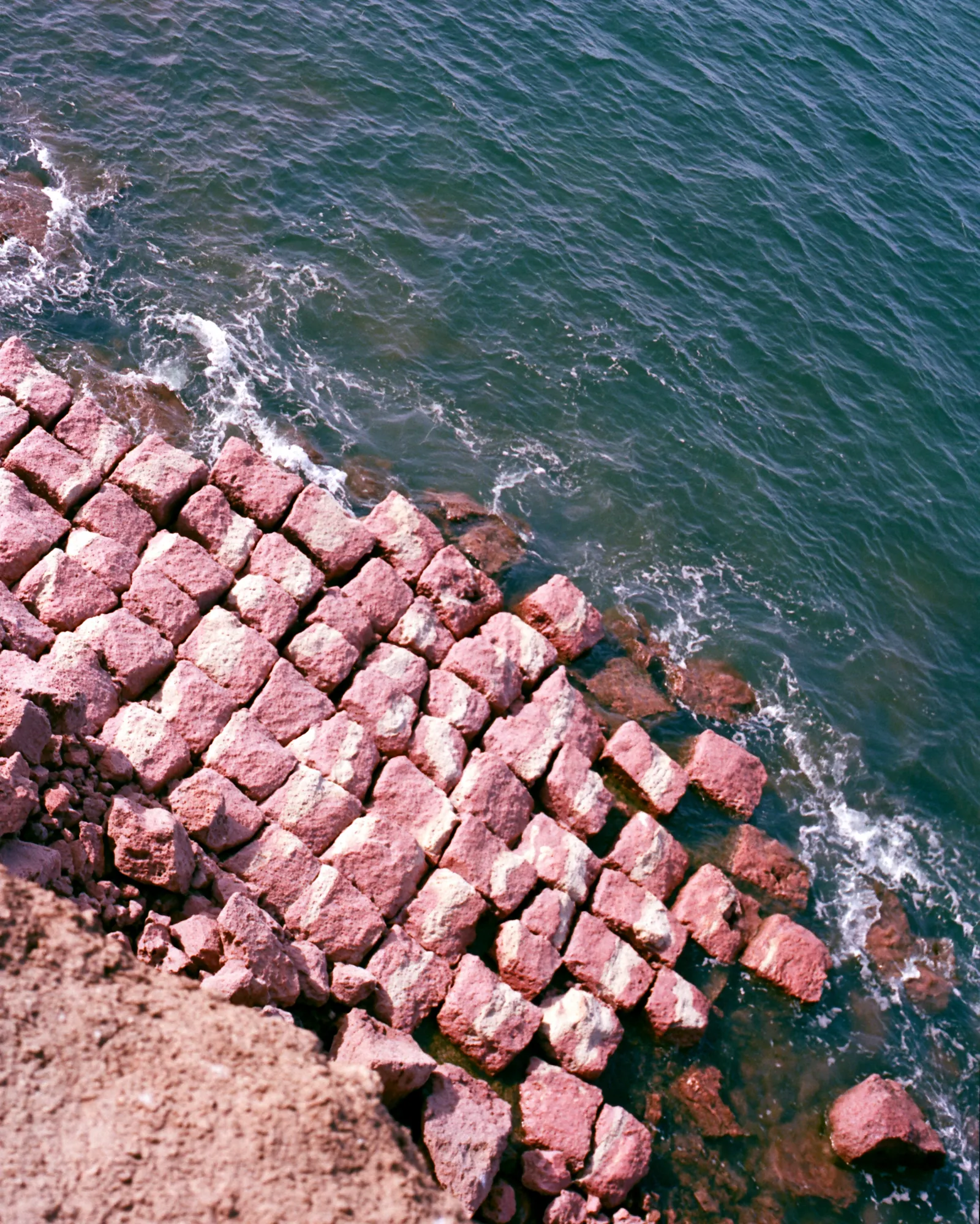 Coral-pink rock blocks stepping down into a deep teal sea, the inspiration for the Taqa Teal & Coral rug