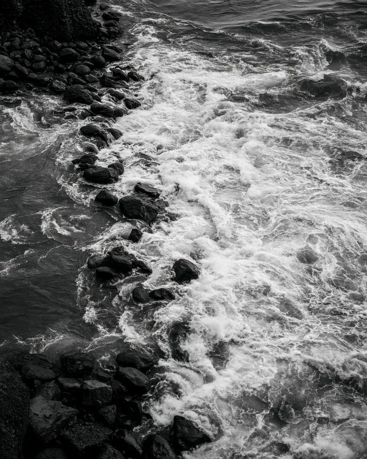Black stones and white foam where fast water breaks over rocks, in black and white
